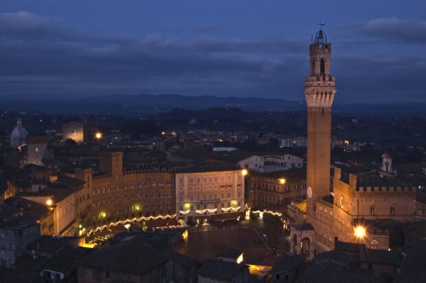 Night view of Siena city with the historic tower and illuminated buildings in evening light