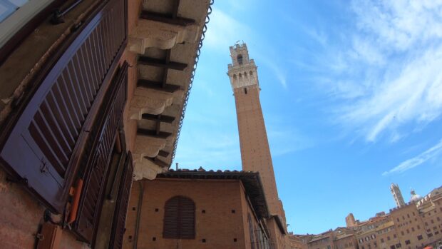 Historic Siena tower with classic shutters under a clear blue sky in Siena
