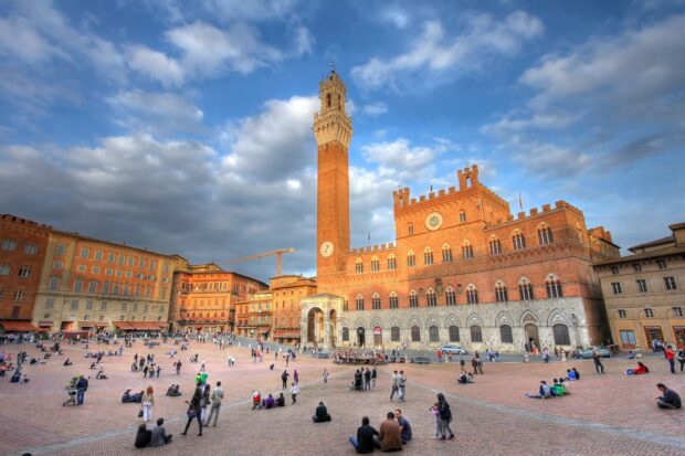 The historic Siena square with ancient brick buildings and a tall clock tower under cloudy sky