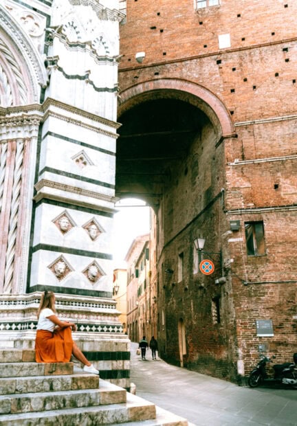 A woman sitting on historic stone steps near Siena architecture and street scene