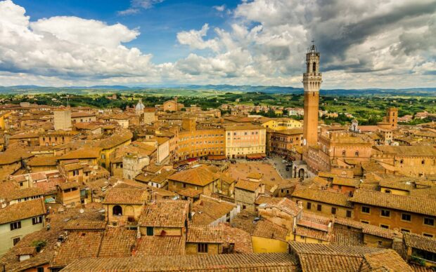 A panoramic view of Siena city with historic buildings and the tall tower under a partly cloudy sky