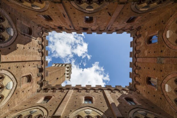 Historic Siena architecture framed by blue sky and clouds viewed from courtyard interior