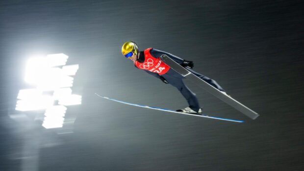 A ski jumper in midair performing a ski jumping competition at night with bright stadium lights