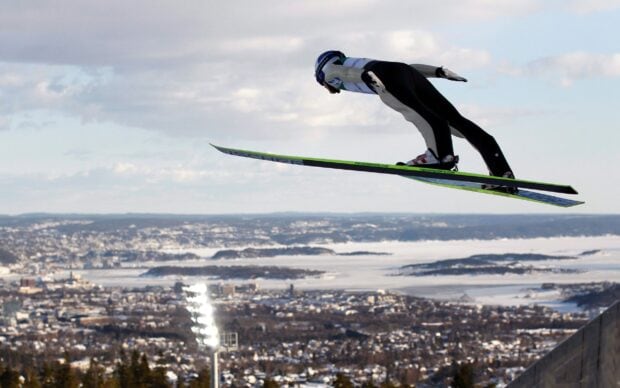 A ski jumper soaring through the air during a ski jumping competition over a cityscape