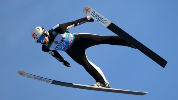 A ski jumper in mid air during a competition against a clear blue sky