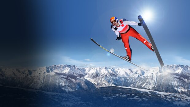 A ski jumper soaring above snowy mountains during a ski jumping competition