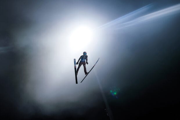 A ski jumping athlete flying through misty air with bright light behind