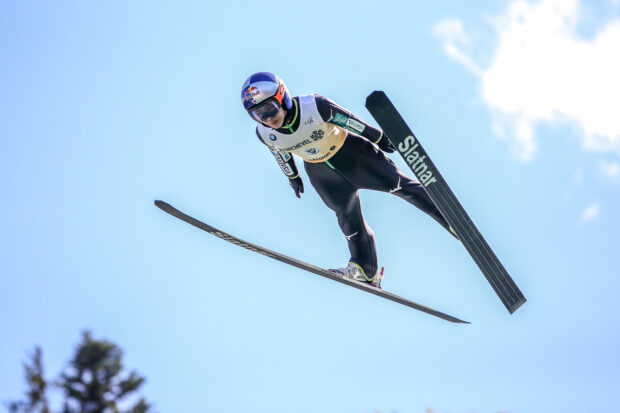 A ski jumping athlete soaring through the air in a competition against a clear blue sky