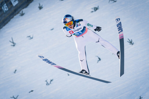 Ski jumper wearing helmet and goggles flying over snow hill in ski jumping sport
