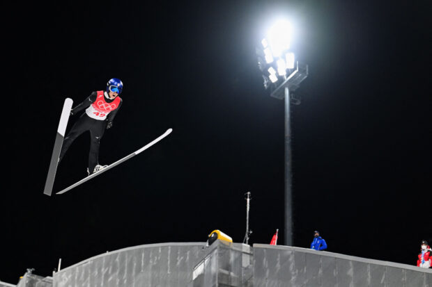 Ski jumping athlete in mid air during night competition under bright stadium lights