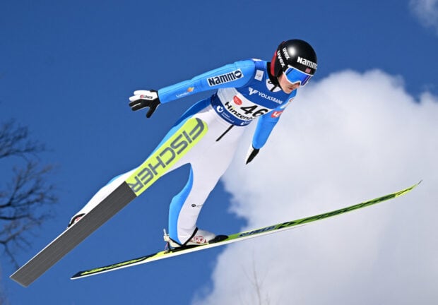 A ski jumper in blue suit flying through the air during a jump under clear skies