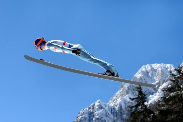 A ski jumper in full flight over snowy mountains during a bright clear day