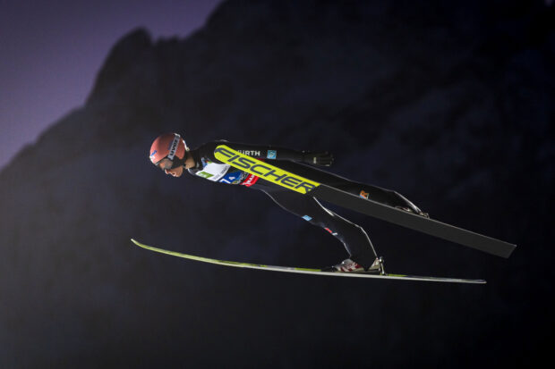 A ski jumper in midair performing a long distance jump during a night competition