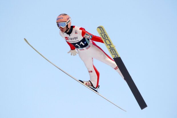 A ski jumper in a red and white suit flying through the air against a clear sky