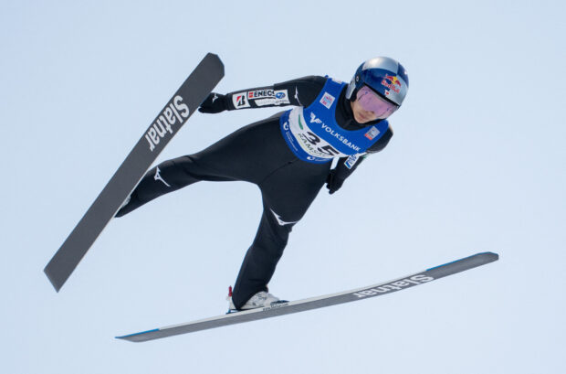 A ski jumper wearing a helmet and suit is soaring in the sky during a ski jumping competition