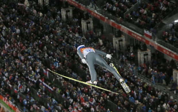 Athlete performing ski jumping in front of a large crowd at the stadium