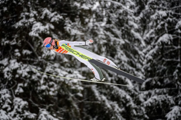 Female ski jumping athlete flying over snowy forest in winter sports competition