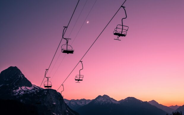 Ski lift lines running across mountain landscape at sunset with a crescent moon visible