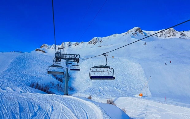 Snowy mountain ski lift with clear blue sky and ski tracks on fresh powder