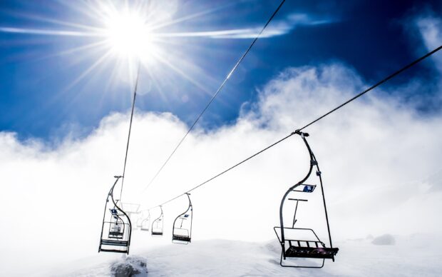 Ski lift carrying empty chairs over a snowy mountain under bright sun rays