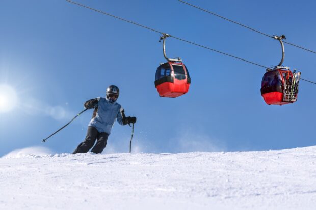 Skier skiing on snow near ski lift under clear blue sky
