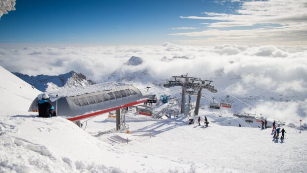 Person Sitting Near Ski Lift at Snowy Mountain with Ski Lift Chairs and Snowy Peaks