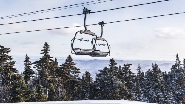 Empty ski lift above snow covered pine trees and mountain range