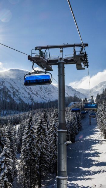 Snow covered ski lift ascending above a winter forest with mountain backdrop