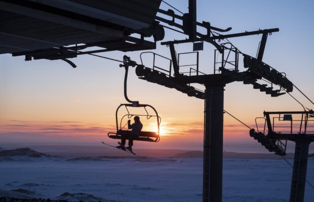 A skier riding a ski lift at sunset over snowy mountain terrain