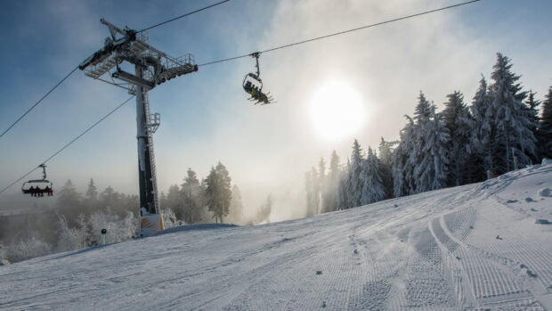 Ski lift with people riding above a snowy slope surrounded by frosted trees and bright sun