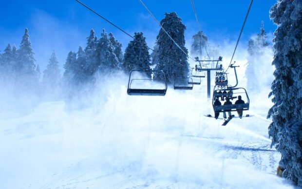 Snow covered trees surround a ski lift carrying skiers up a snowy mountain slope