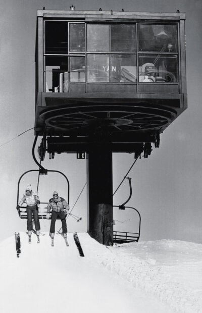 Two skiers riding a ski lift on snowy mountain slopes in winter