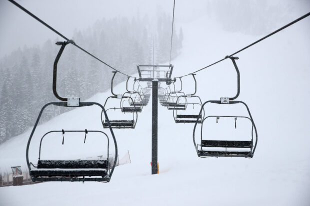 Empty ski lift chairs moving over snowy ski slopes in winter forest