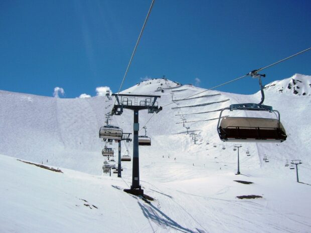 Ski lift carrying passengers over the snowy mountain slopes against a clear blue sky