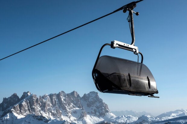 Ski lift hanging over snowy mountains under a clear blue sky
