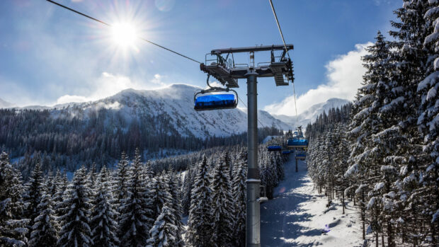 Ski lift surrounded by snow covered trees and mountains under a bright sunny sky