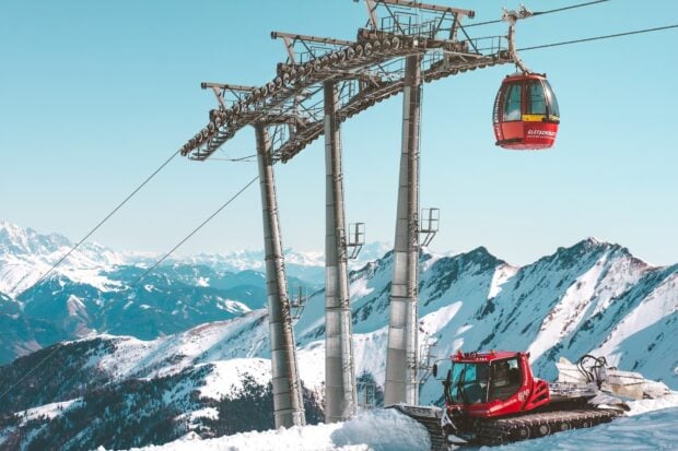 A ski lift carrying passengers up snowy mountain peaks under clear blue sky