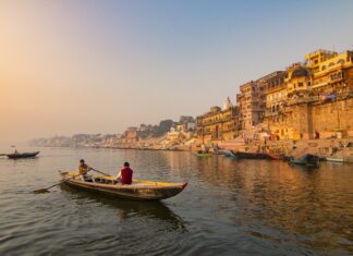 Skiff on river near ancient city buildings during sunset