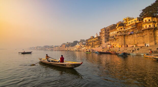 Skiff on river near ancient city buildings during sunset