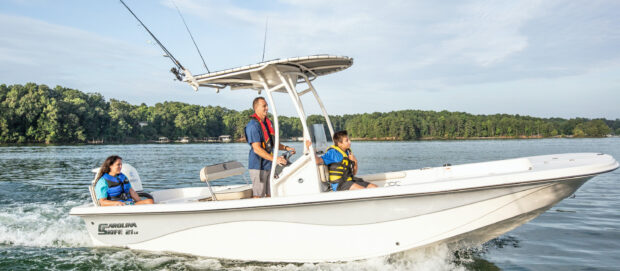 A man and two children riding a Carolina skiff on calm water with trees in the background