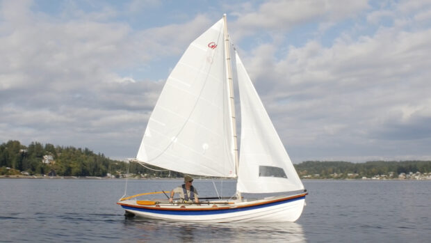 A man sailing a traditional skiff boat on calm water under cloudy sky