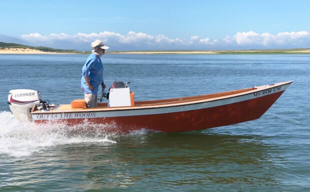 Man steering a skiff on calm water under clear skies