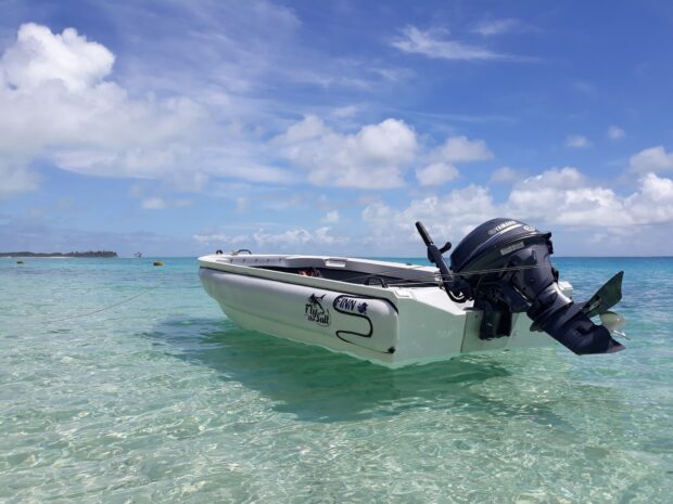 A skiff floating on clear shallow water under a blue sky with scattered clouds