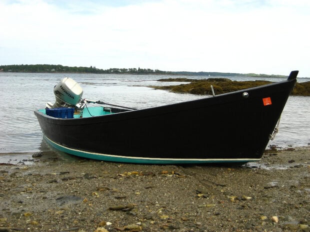 A black skiff with a Honda motor parked on a rocky shore near the water