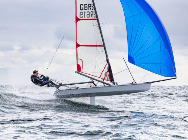 A skiff sailing fast on the ocean with a blue sail and a man controlling the boat