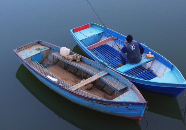 A man sitting in a skiff on calm water during the early morning