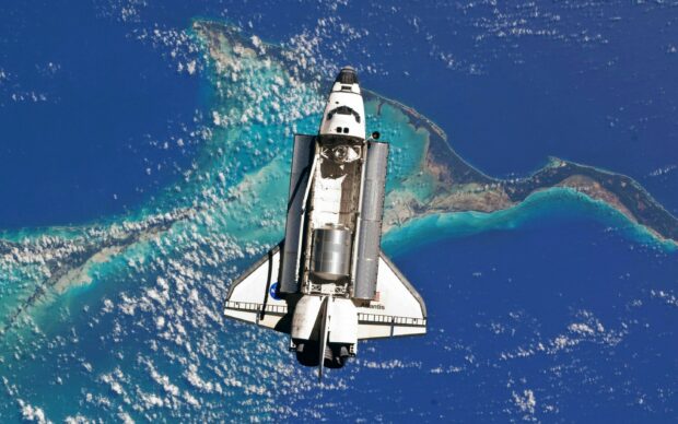 Space shuttle Atlantis orbiting above a vibrant island in the ocean viewed from space