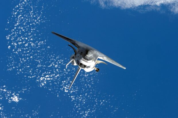 Space shuttle flying above clouds in the sky with blue background