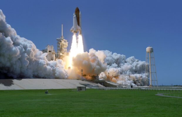 Space shuttle launch with thick smoke rising against a clear blue sky