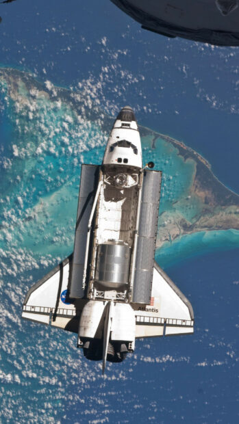 Space shuttle orbiting above the ocean near a tropical island with clear blue water
